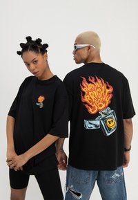 Two models wear black oversized tees with graphic lighters; one shows front logo, the other shows large back design with flames and text.