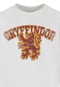 Fehér póló, amelyen egy megkopott piros és arany Griffendél oroszlán embléma látható, felette a "GRYFFINDOR" szó látványos, ívelt betűtípussal.