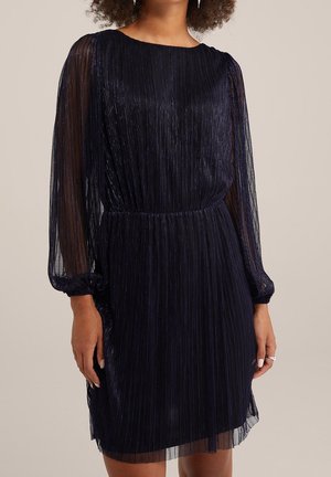 Robe plissée bleu marine avec manches longues transparentes, taille élastique et encolure ronde. Le tissu texturé ajoute un léger éclat.