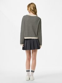 Femme vue de dos portant un pull rayé noir et blanc, une jupe plissée foncée, des chaussettes blanches à rayures noires, et des baskets blanches.