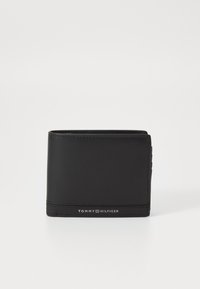 Portefeuille en cuir noir avec une texture lisse, design pliable en deux, et logo en relief "TOMMY HILFIGER" à l'avant. Slim avec des emplacements pour cartes sur le côté.