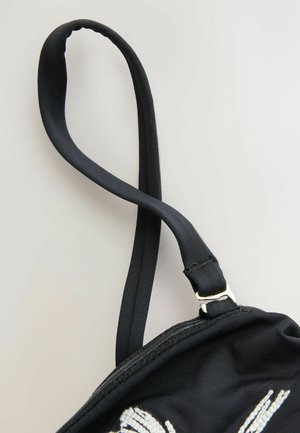 Borsa di stoffa nera con una finitura texturizzata. Presenta una tracolla nera con un gancio di metallo dorato e un dettaglio ricamato in bianco.