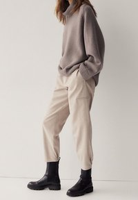 Pantalons cargo beiges avec des poignets élastiques, associés à un pull col roulé gris clair et des bottines noires. Textures douces et coupe détendue.
