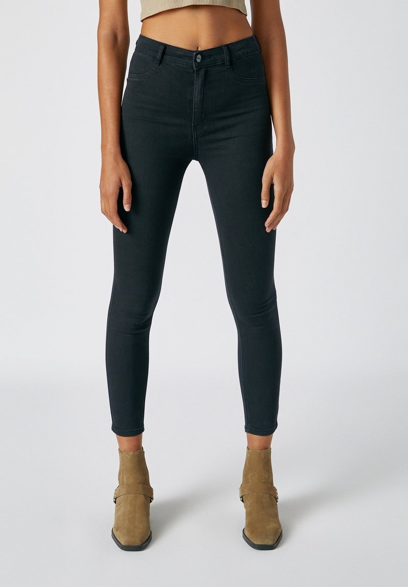 Vaqueros skinny negros de cintura alta. Confeccionados en denim con una textura suave. Presentan un cierre con botón y cinco bolsillos. Botines marrones a la vista.