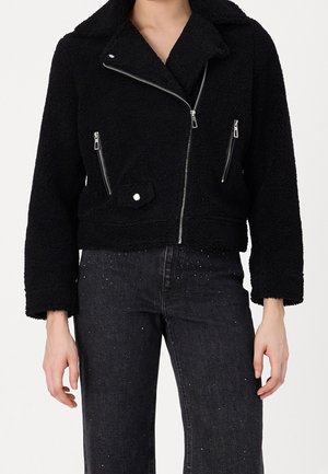 Veste en polaire noire zippée avec col large portée avec un jean noir taille haute présentant un motif discret de taches blanches.