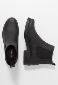 Botas negras hasta el tobillo hechas de cuero suave con paneles laterales elásticos, una suela de goma texturizada y un tacón bajo y cuadrado. Marca visible en el interior.
