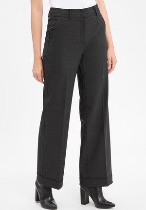 Zwarte, wijde broek met een gladde textuur, voorzien van een persvouw aan de voorkant en omgeslagen zomen. Gecombineerd met textuur, zwarte hoge laarzen.