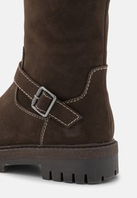 Καφέ σουέντ μποτάκι με ασημί ζώνη, αντίθετο ράψιμο και υφασμένο μαύρο καουτσούκ σόλα με βαθύ προφίλ.