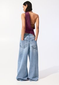 Haut violet sans dos avec un design drapé, associé à un jean en denim bleu clair à jambes larges doté de grandes poches arrière.