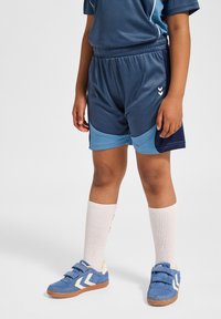 Blå sportshorts med ljusblå detaljer, som bärs med vita knästrumpor och blå skor med kardborreband och ett mönstrat design.