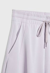 Joggers de color lavanda claro con un tejido suave, cintura elástica con cordón y bolsillos laterales. Detalle de costura sutil a lo largo de las costuras.