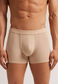 Beige boxer briefs with a smooth, stretchy fabric, featuring a contoured front pouch and a soft, elastic waistband. No visible patterns.