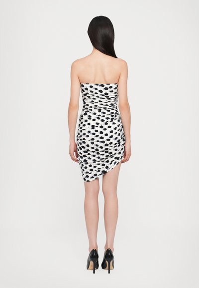 Strapless minidress in het wit met een zwart stippenpatroon, gerimpeld ontwerp, asymmetrische zoom en gecombineerd met zwarte hoge hakken.
