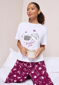 Hvid t-shirt med "French Breakfast Club" grafik og lyserøde accenter, parret med bordeaux pyjamasbukser med morgenmadstema mønstre.