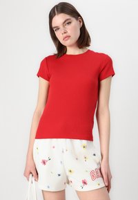 Rød ribbet kortærmet top parret med hvide shorts med blomstermønster og rød tekst. Glat tekstur på begge beklædningsgenstande.