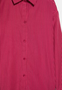 Rød og lyserød lodret striped skjorte med krave, lange ærmer og fire synlige knapper ned foran.