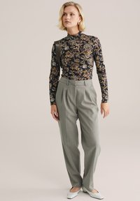 Crna cvjetna bluzica dugih rukava, sive hlače visokog struka i bijele ravne cipele. Bluza ima lažni ovratnik; hlače imaju nabore.