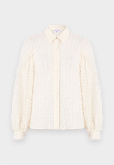 Valge pluus tekstureeritud ruudustikuga, millel on krae, nööbiväli ees ja puffi varrukad elastsete mansettidega. Kerge ja õhuline materjal.