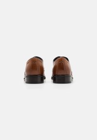 Chaussures en cuir marron avec une finition lisse, bout rond, couture décorative et un talon noir ; logo embossé à l'arrière.
