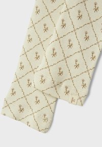 Krēma krāsas audums ar teksturētu ribu rakstu, kurā ir dimanta prints ar maziem ziedu motīviem bēšā krāsā. Marķējums apakšējā malā.