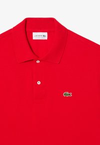 Röd bomullspolo med klassisk krage, tvåknapps knäppning och grön krokodil-logotyp broderad på vänster bröst.