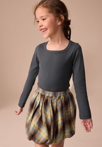 Maglia grigia a maniche lunghe con scollatura a girocollo abbinata a una gonna a palloncino a quadri in blu, giallo e marrone, con vita elasticizzata.