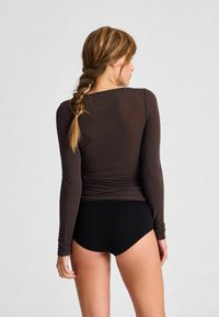Tmavo hnedý top s dlhými rukávmi, priliehavý strih, hladká textúra a zberané detaily na zadnej strane, v kombinácii s čiernymi chlapčenskými šortkami.
