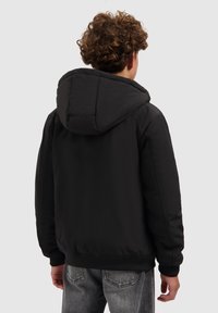 Zwarte gevoerde jas met capuchon, voorzien van geribbelde manchetten en zoom. Gladde textuur en eenvoudig ontwerp, met minimale details.