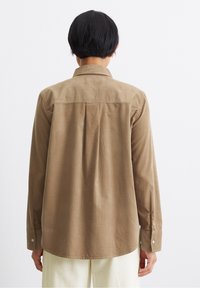 Braun langärmliges Shirt mit Yoke-Design, weichem Baumwollstoff, Rückenfalte für den Sitz und knöpfbaren Manschetten. Glatte Textur, abgerundeter Saum.