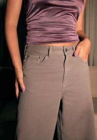 Szare spodnie o szerokich nogawkach z teksturowanej tkaniny, z bocznymi kieszeniami i widocznymi szwami. Połączone z dopasowanym, błyszczącym fioletowym topem.