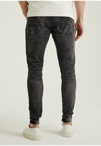 Jeans de mezclilla negra con un lavado descolorido. Cuenta con dos bolsillos traseros, un ajuste slim y un ligero desgaste en los dobladillos. Combinados con zapatillas blancas.