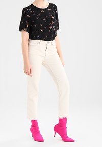 Top negro de manga corta con estampado floral colorido, combinado con jeans recortados de color claro y botas de tacón alto rosas con diseño arrugado.