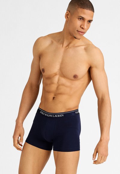 Marineblauwe boxershorts van katoen, met een logo-elastische band en een aansluitend ontwerp. Model poseert met een atletisch figuur.