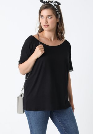 Zwarte korte mouwen top met een brede halslijn en kantdetails. Gecombineerd met medium-wash denim jeans en een zilveren rechthoekige handtas.