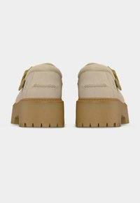 Μπεζ πλατφόρμες από σουέντ με παχιά σόλα από καουτσούκ, εμφανιζόμενες από πίσω με φόντο λευκό.