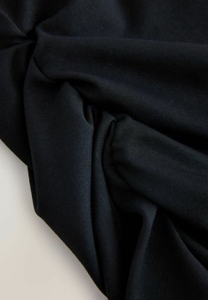 Melna auduma virsma ar redzamām faktūrām un krokām, radot mīkstas ēnas un gaismas atspīdumus uz gaišas virsmas.