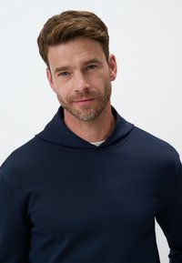 Felpa con cappuccio blu navy in un tessuto morbido e liscio. Presenta una vestibilità comoda e cuciture sottili lungo i bordi.