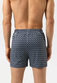 Shorts de bain bleu marine à motifs avec un tissu léger, présentant de petits dessins graphiques blancs, une taille élastique et une coupe ajustée.