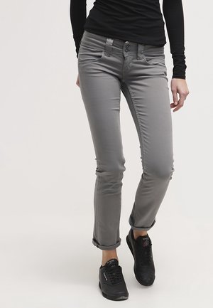 Person wearing fitted grey pants with rolled cuffs and black Reebok sneakers, standing against plain background.