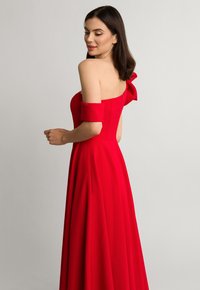 Czerwona wieczorowa sukienka z odkrytymi ramionami i detalem w postaci kokardy. Lekka tkanina, dopasowana góra i pełna spódnica. Zamek błyskawiczny z tyłu.