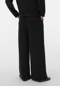 Pantalon noir à jambes larges avec une finition douce et texturée, doté de deux poches et d'une coupe décontractée, associé à des ballerines à motifs.