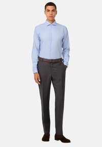 Camicia azzurra a maniche lunghe con bottoni abbinata a pantaloni a quadri grigio scuro e scarpe in suede marroni. Cintura in pelle marrone completa l'outfit.