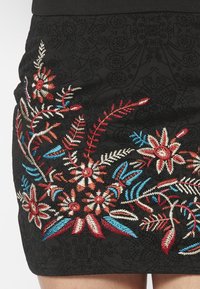 Svart kjol med flerfärgad blommig broderi i röd, blå och krämfärgad. Bakgrunden innehåller intrikata texturerade mönster.