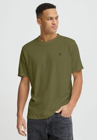 T-shirt verde oliva a maniche corte in tessuto morbido, con scollatura rotonda e un piccolo logo scuro sul lato sinistro del petto.
