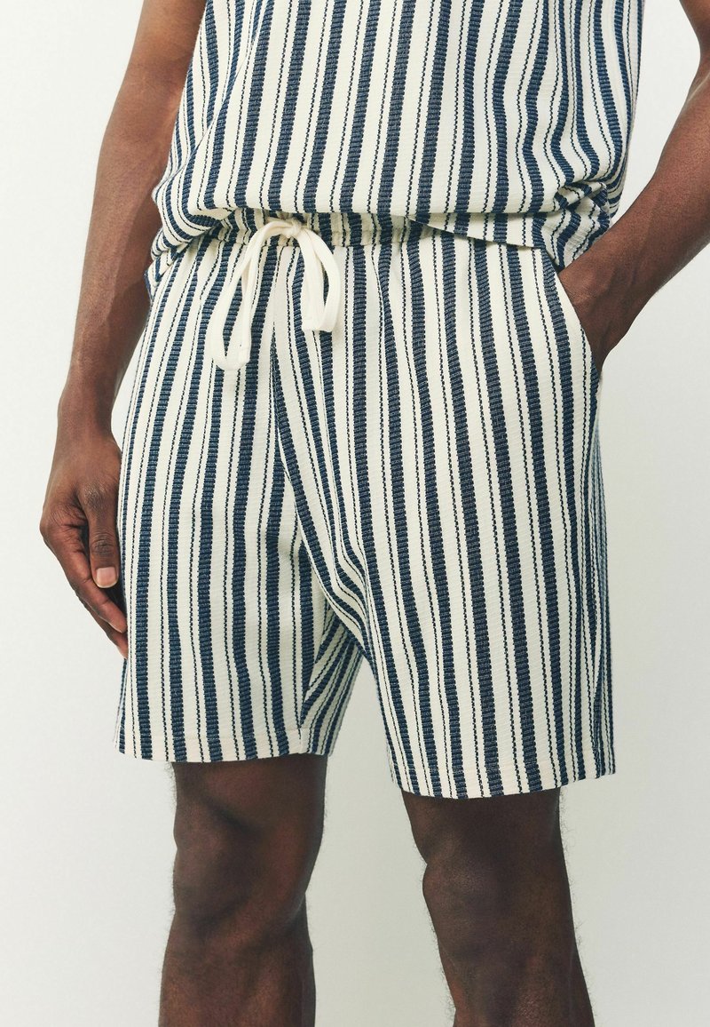 Shorts rayés avec un schéma de couleurs blanc et marine, taille élastique avec cordon de serrage, et poches latérales, fabriqués en tissu léger.