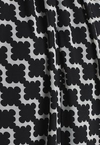 Tissu à motif arborant un design floral noir répété sur un fond blanc, avec une texture de tissu et des plis visibles.