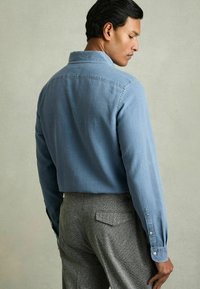 Cămașă cu guler, de culoare albastru deschis, cu mâneci lungi și textură netedă, asortată cu pantaloni gri cu textură.