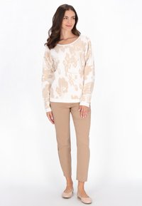 Sweter dziany w kremowym kolorze z beżowym wzorem kwiatowym, zestawiony z beżowymi spodniami slim-fit i jasnymi płaskimi butami. Prosty, codzienny design.
