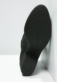 Suela de bota negra con superficie de goma texturizada, forma redondeada, tacón definido y detalles de costura a lo largo de los lados.
