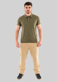 Polo shirt vert olive avec un col, trois boutons, associé à un pantalon cargo kaki avec des poches avant, et des baskets noires avec des accents clairs.